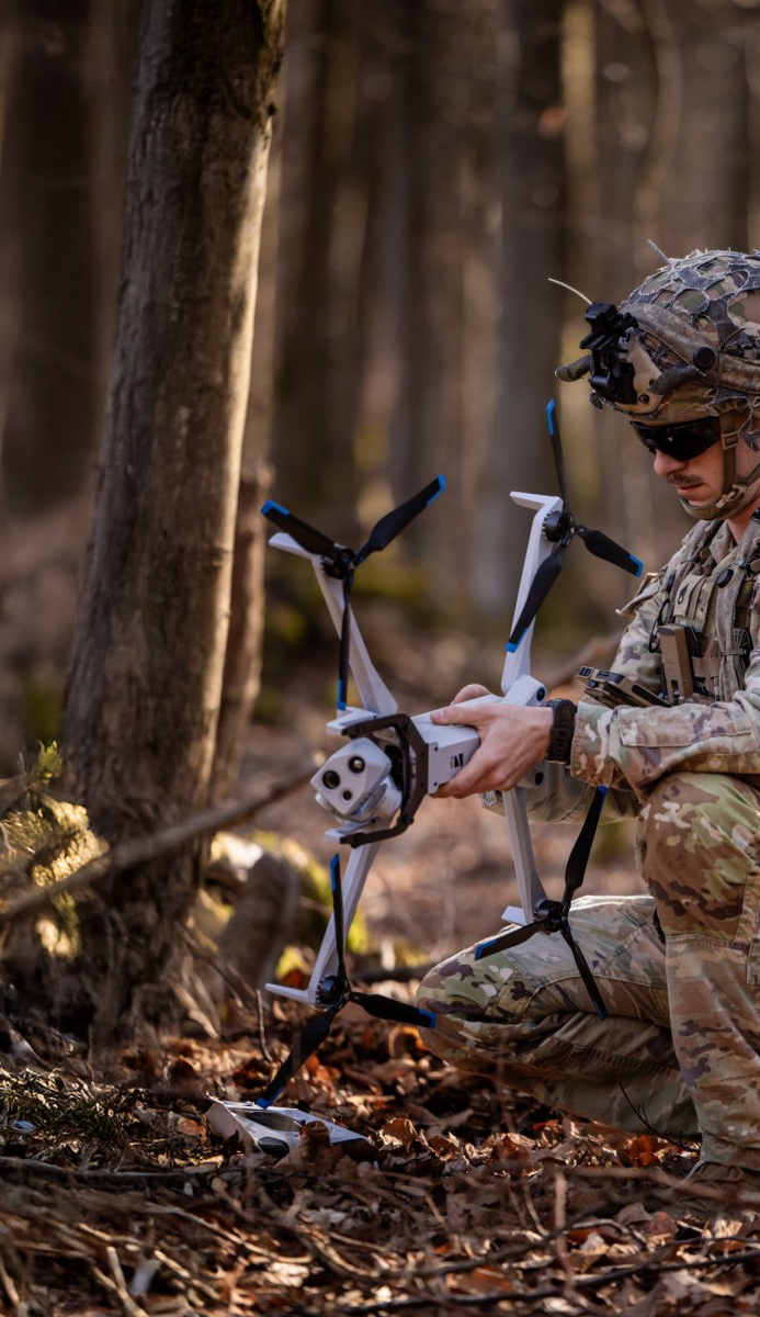 crouching warfighter in the woods with a Skydio X10D drone in hand
